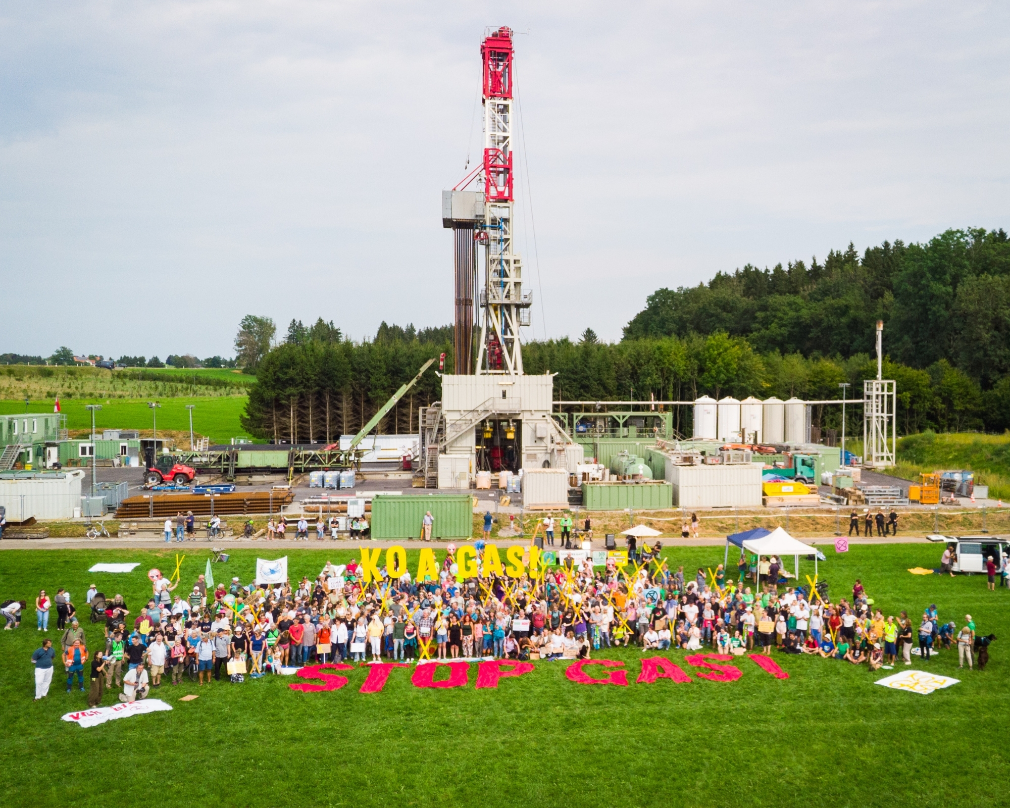 Eine große Menschenmenge vor einem Gasbohrturm in Reichling mit großen Buchstaben die einmal "Koa Gas!" und "Stop Gas!" bilden